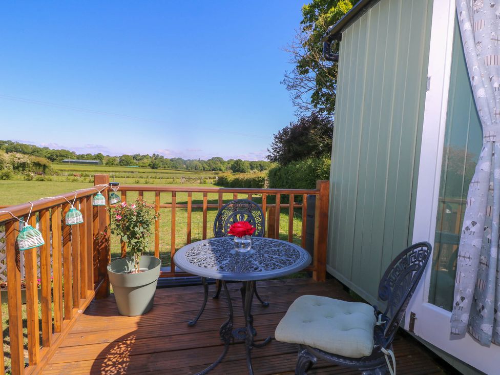 A wooden deck with a metal table and two chairs overlooking a green field at Songbirds in St Michaels Kent