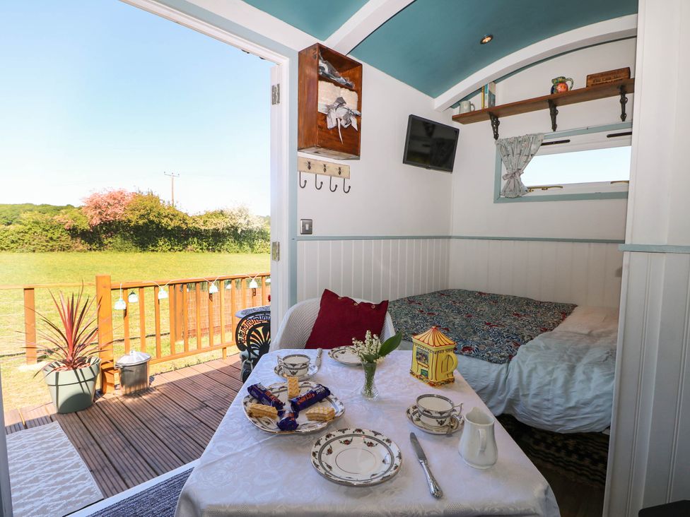A small room with a bed a table set with china tea cups and plates and an open door leading to a wooden deck with a potted plant and a grassy field at Songbirds in St Michaels Kent