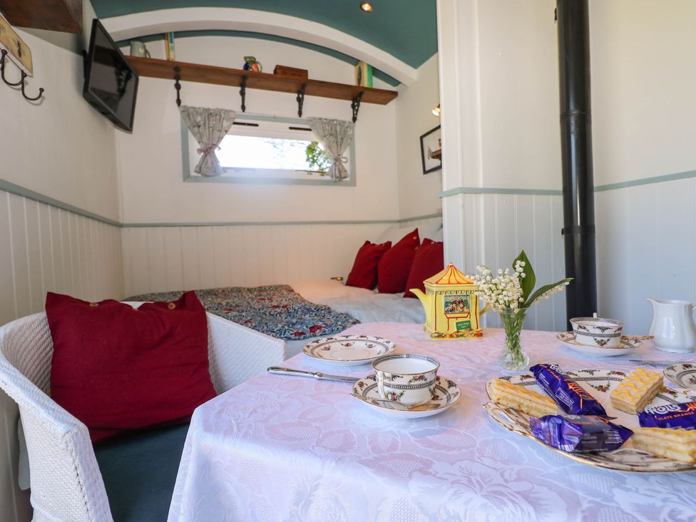 A small dining area with a table set for tea and snacks a corner daybed with red cushions and a window above at Songbirds St Michaels Kent