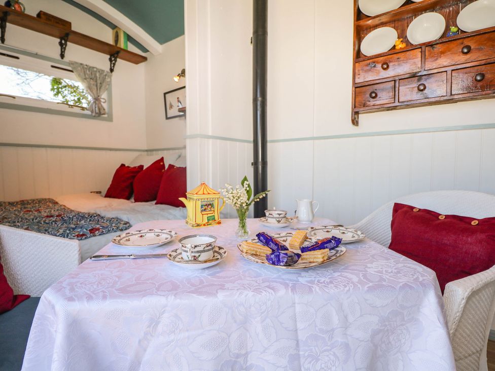 A small dining area with a table set for tea including cups and snacks a cushioned seating area with red pillows and a mounted wooden cabinet with plates in Songbirds St Michaels Kent
