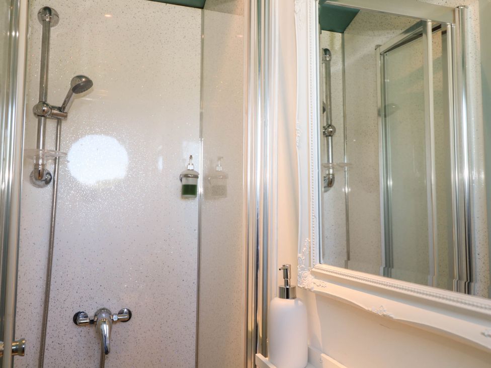 A shower area with a showerhead soap dispensers and a mirror with a white frame at Songbirds in St Michaels Kent