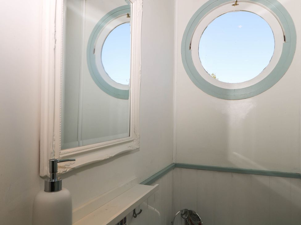 A small room with a round window painted with blue trim a white framed mirror and a white soap dispenser on a shelf at Songbirds in St Michaels Kent