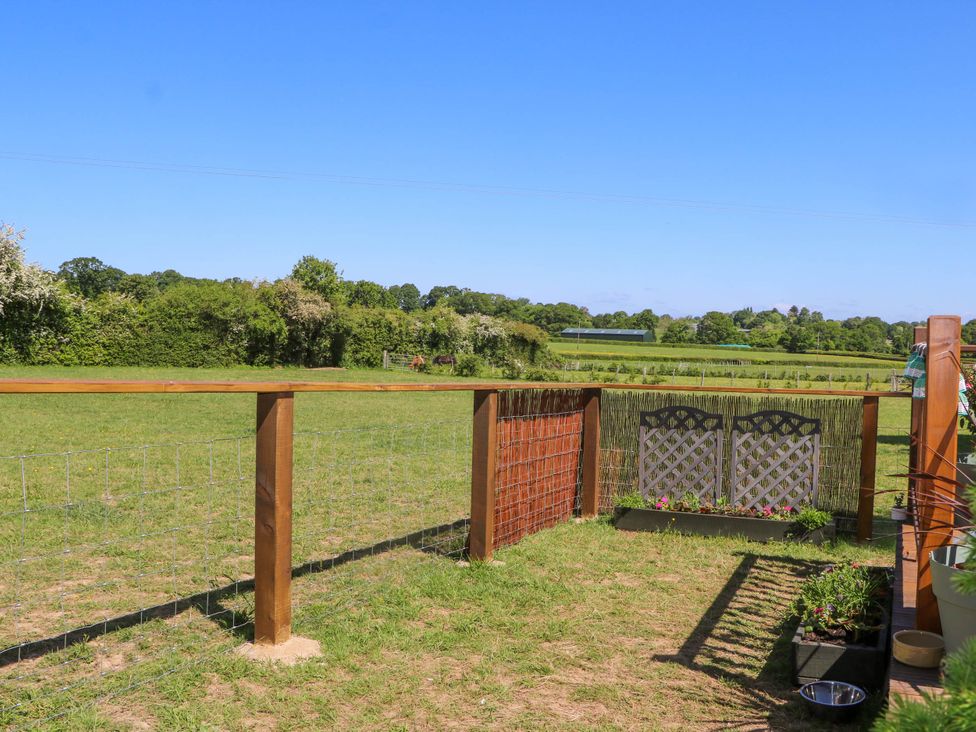 A fenced grassy patio area with planters and a view of fields and trees at Songbirds in St Michaels Kent
