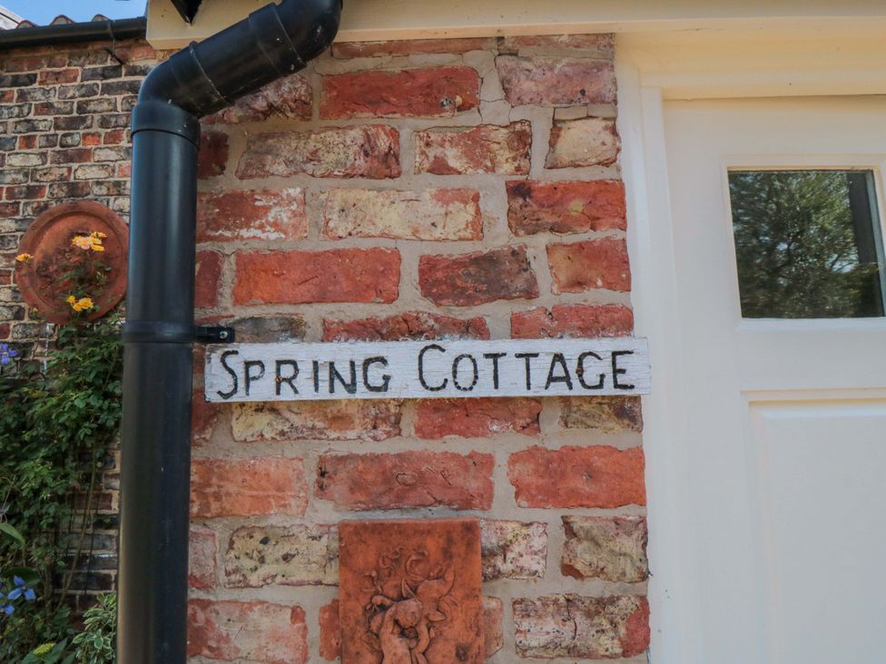 A sign labeled Spring Cottage attached to a brick wall with flowers at Spring Cottage in York