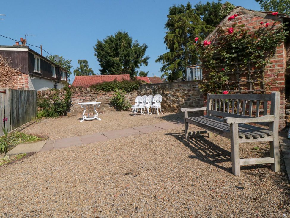 A garden with a wooden bench and white chairs at Spring Cottage in York