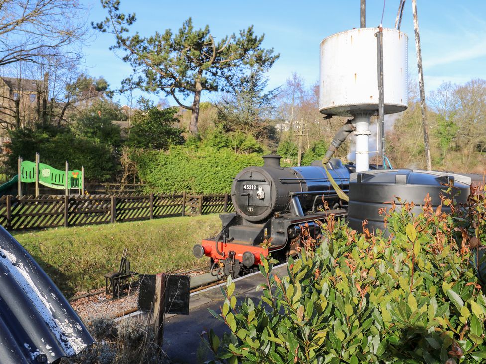 A steam locomotive by a water tank near playground equipment at Loco Lodge in Keighley