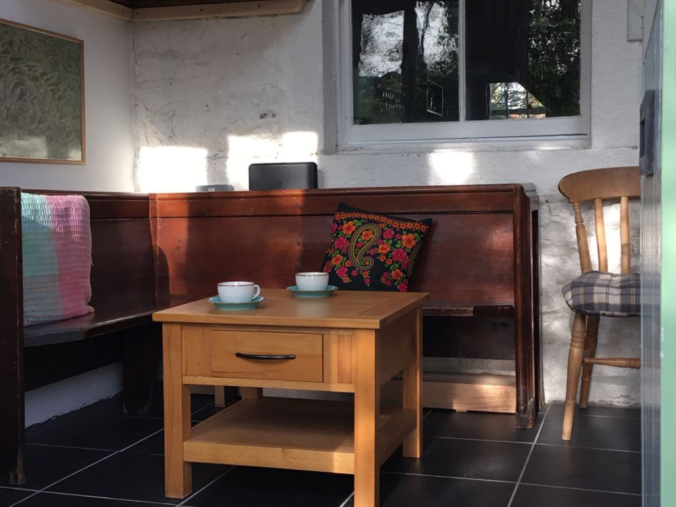 A corner seating area with wooden benches a wooden chair a small wooden table and two cups at Doffers Cottage in Airton