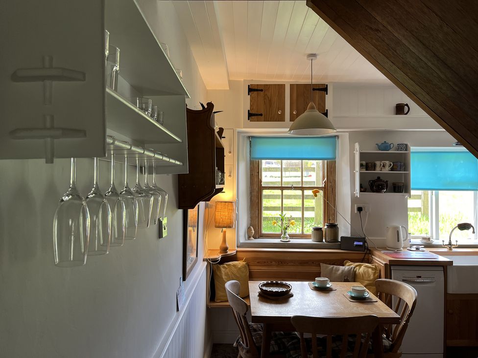 A kitchen dining area with wooden table and chairs near windows with blue blinds at Doffers Cottage in Airton