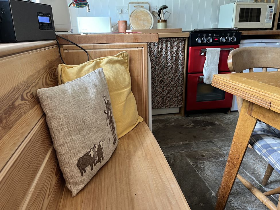 A kitchen corner with wooden bench seating with cushions a red oven microwave and wooden dining table at Doffers Cottage in Airton