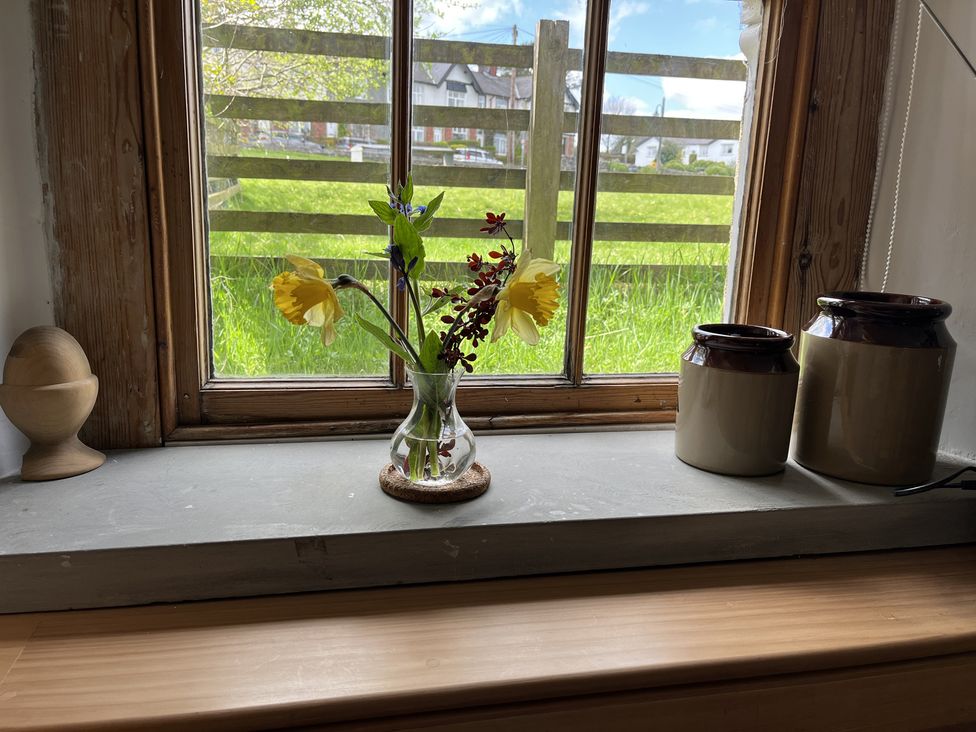 A window with wooden frame and ledge holding a glass vase with flowers two ceramic jars and a wooden egg-shaped object at Doffers Cottage in Airton