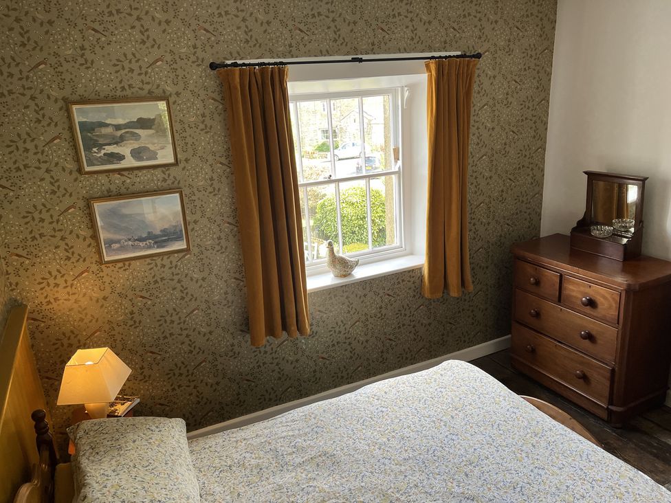 A bedroom with a bed a window with curtains a wooden dresser and framed pictures at Doffers Cottage in Airton