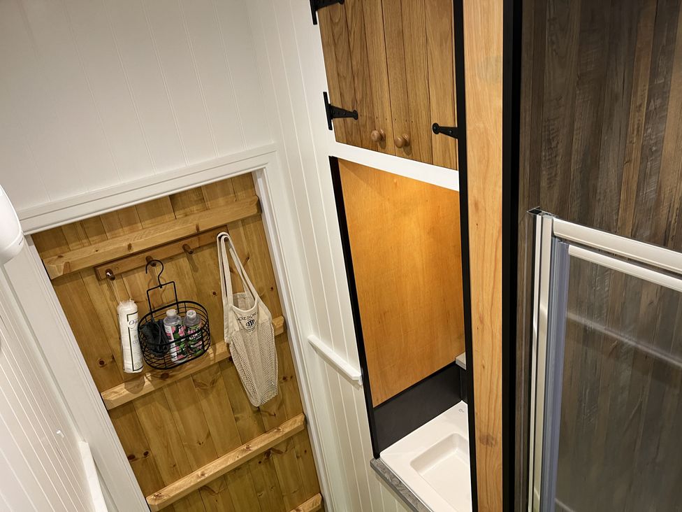 A wooden door with hooks holding bags and bottles next to a small sink and shower area at Doffers Cottage in Airton