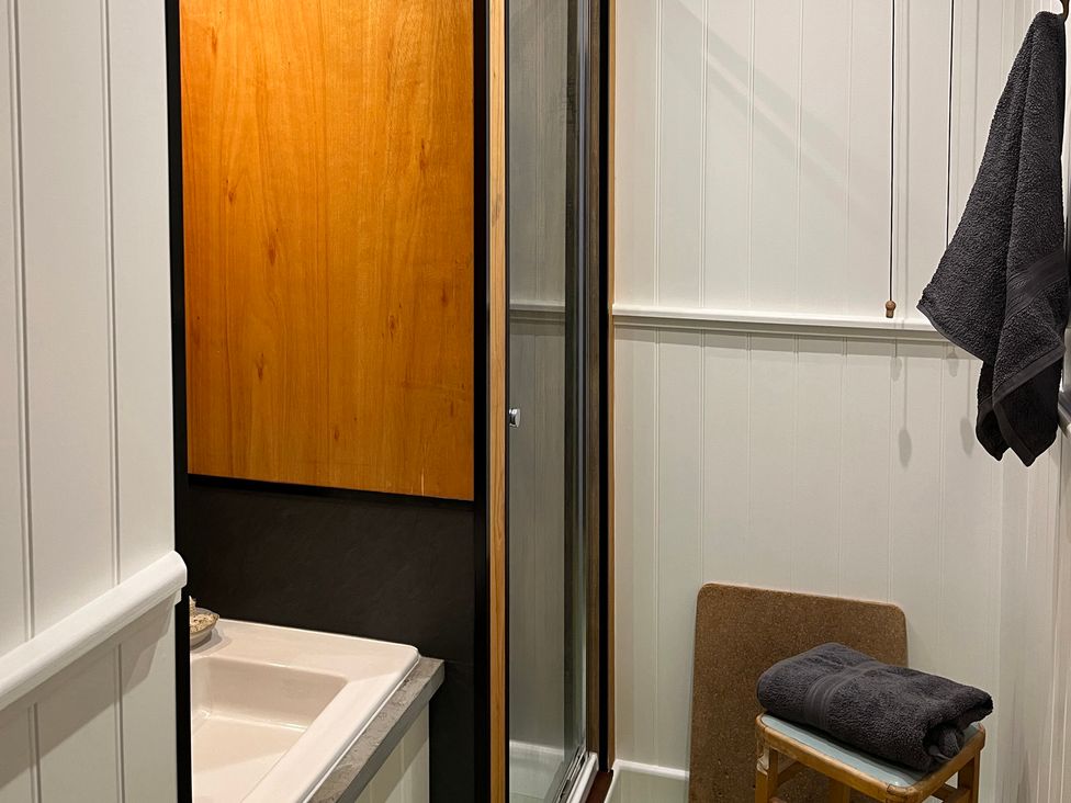 A bathroom with a sink partial view a shower with glass door a towel hanging and another towel on a chair at Doffers Cottage in Airton