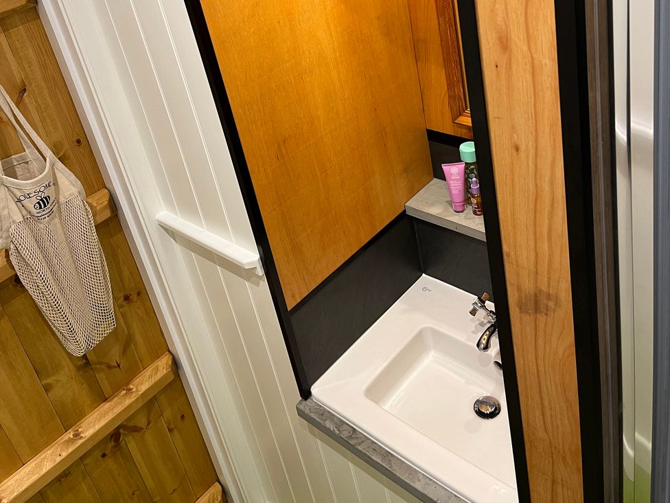 A small bathroom sink with a faucet and countertop with toiletries next to wooden and white paneled walls at Doffers Cottage in Airton