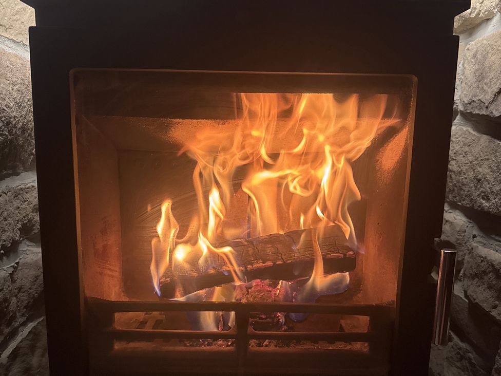 A fireplace with flames and burning wood logs at Yew Tree Cottage