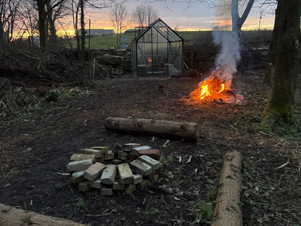 An outdoor area with a fire pit and a greenhouse at Yew Tree Cottage Mealsgate near Ireby