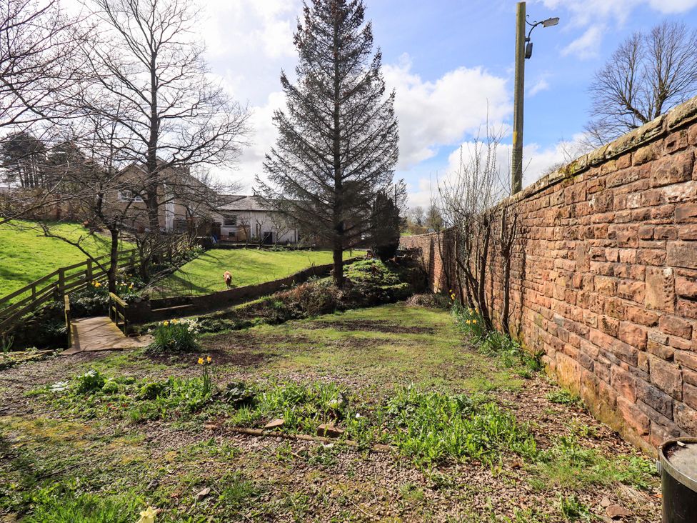 A garden with trees and a wooden bridge at Yew Tree Cottage Mealsgate near Ireby