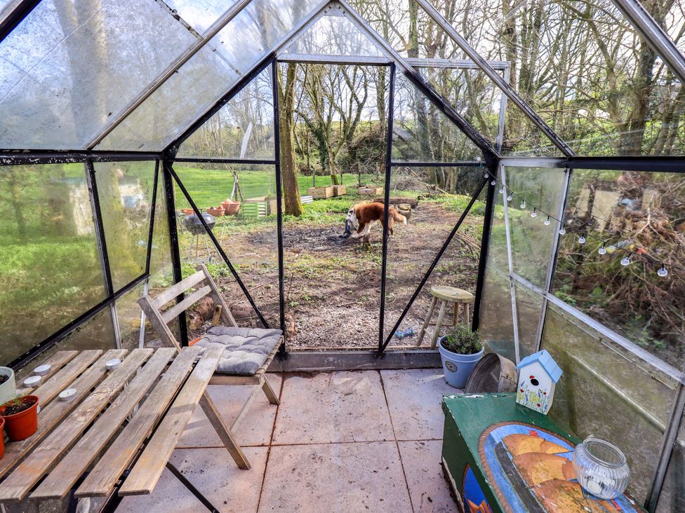 A greenhouse with a table and a dog outside at Yew Tree Cottage Mealsgate near Ireby