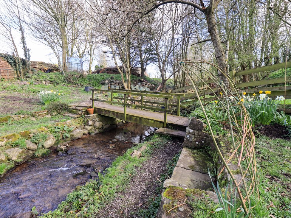 A garden with a wooden bridge over a stream at Yew Tree Cottage Mealsgate near Ireby