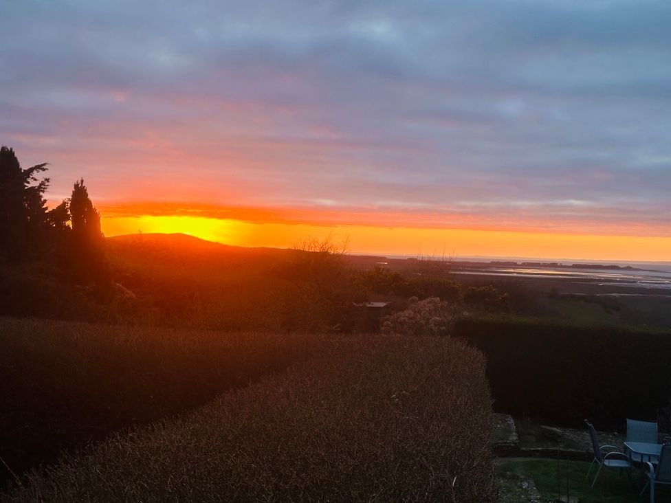 A view of a sunset over the sea with trees and a garden at Burry House in Llanmorlais