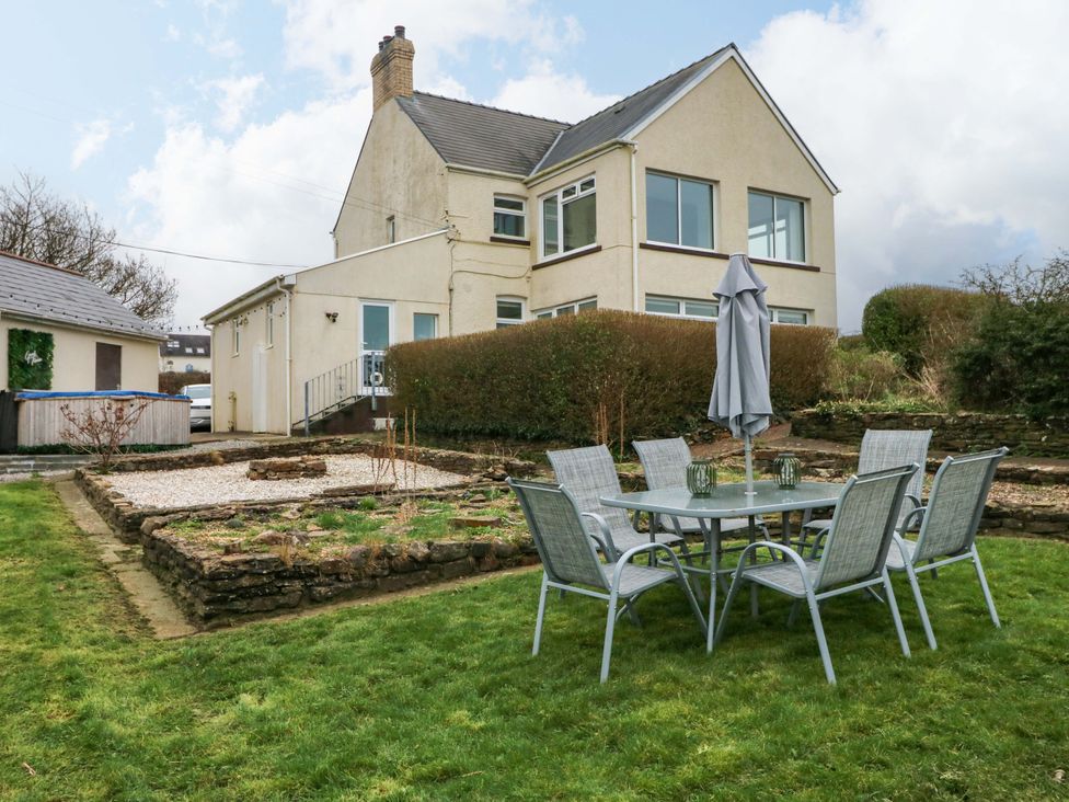 A house with a table and chairs under an umbrella in the garden at Burry House in Llanmorlais