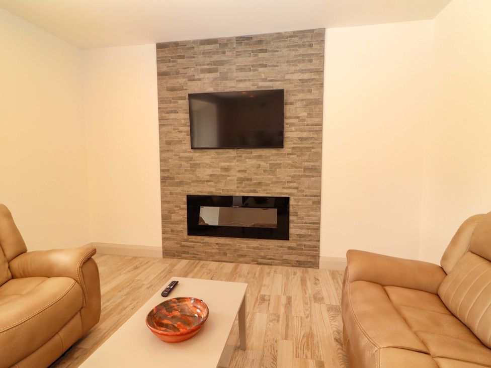 A living room with a TV mounted on a wall and a fireplace at Teach Ti in Miltown Malbay