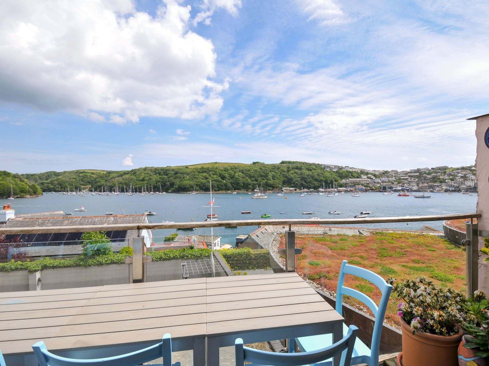 A balcony with a table and blue chairs overlooking boats on a river and hills at 5 Esplanade in Fowey