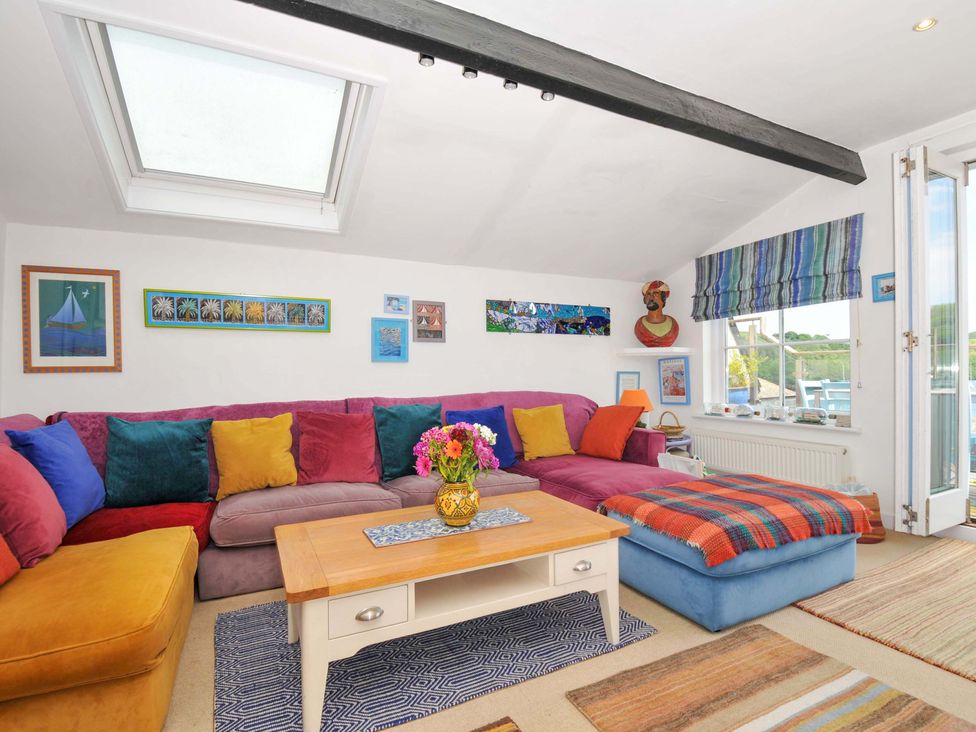 A living room with a colorful sectional sofa cushions a wooden coffee table and a blue ottoman by a window at 5 Esplanade in Fowey