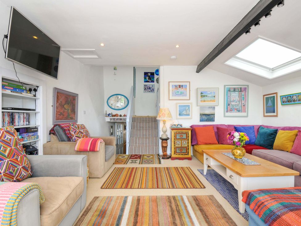 A living room with a striped carpet a wooden coffee table a colorful sectional sofa and framed pictures on the walls at 5 Esplanade in Fowey