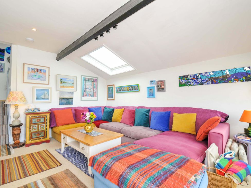 A living room with a large sectional sofa with colorful cushions and a wooden coffee table under a skylight at 5 Esplanade in Fowey