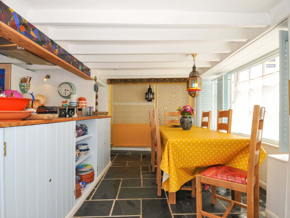 A kitchen and dining area with a yellow polka dot tablecloth on a wooden table and wooden chairs with patterned cushions at 5 Esplanade in Fowey
