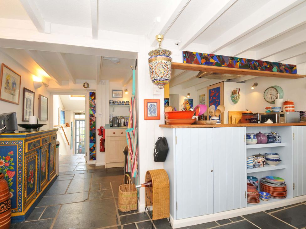 A kitchen area with shelves of dishes and utensils next to a hallway with a decorated sideboard at 5 Esplanade in Fowey