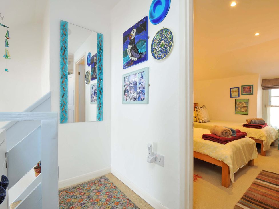 A hallway with a mirror and wall decorations leading to a bedroom with two single beds with towels on them at 5 Esplanade in Fowey
