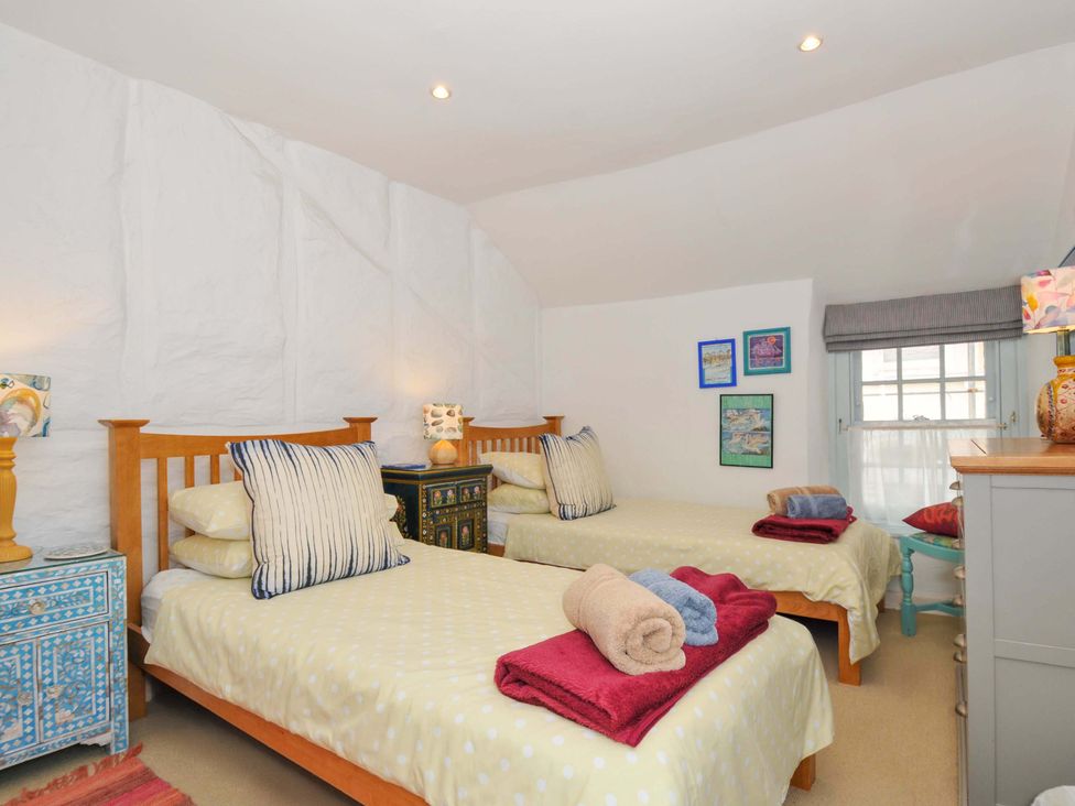 A bedroom with two single beds with folded towels on each bed bedside tables lamps and framed pictures on the wall at 5 Esplanade in Fowey