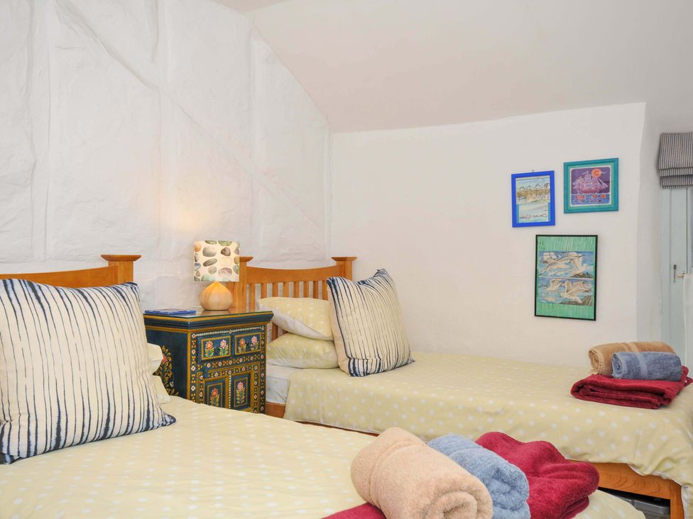 A bedroom with two single beds, a painted nightstand with a lamp, and framed pictures on the wall at 5 Esplanade in Fowey