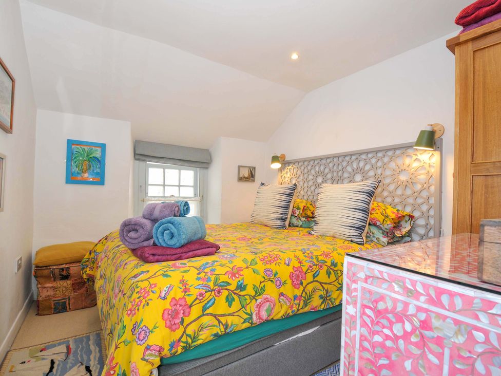 A bedroom with a bed with a yellow floral bedspread and rolled towels on top at 5 Esplanade in Fowey