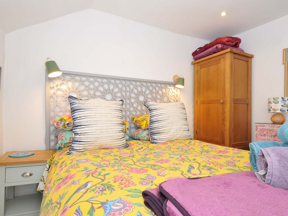A bedroom with a bed with floral bedding and striped pillows next to a wooden wardrobe at 5 Esplanade in Fowey