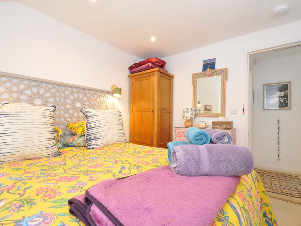A bedroom with a bed featuring floral bedding and striped pillows and folded towels on the bed near a wooden wardrobe and a dresser with a mirror at 5 Esplanade in Fowey