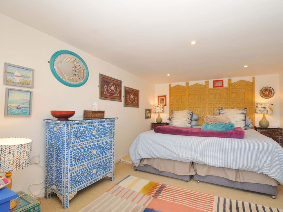 A bedroom with a double bed and patterned bedding a blue decorated chest of drawers and wall art at 5 Esplanade in Fowey