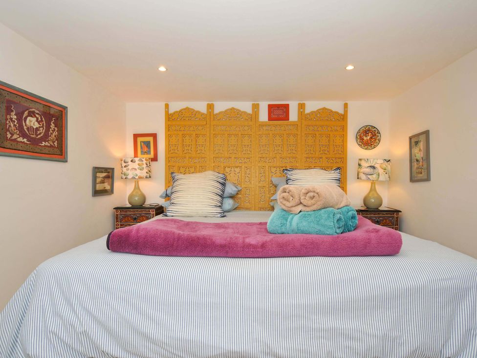 A bedroom with a bed featuring striped bedding and rolled towels on top with a decorative yellow headboard and lamps on bedside tables at 5 Esplanade in Fowey