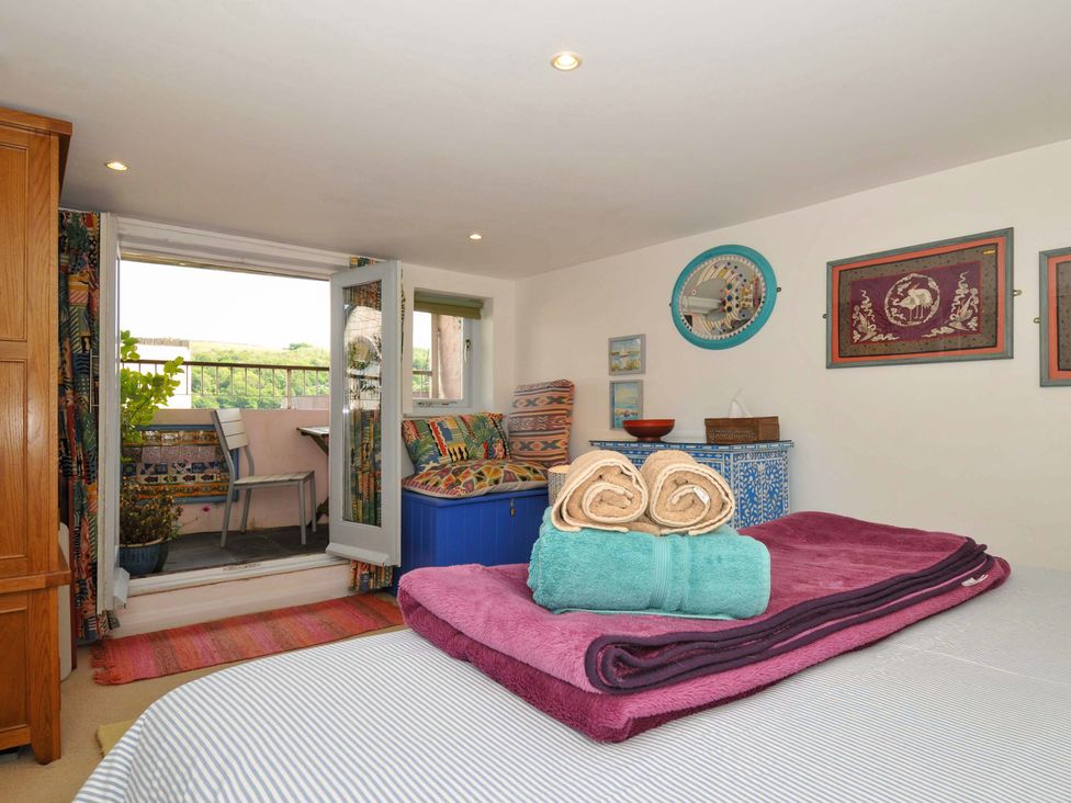 A bedroom with a bed with towels and blankets on it and a small balcony with a chair at 5 Esplanade in Fowey