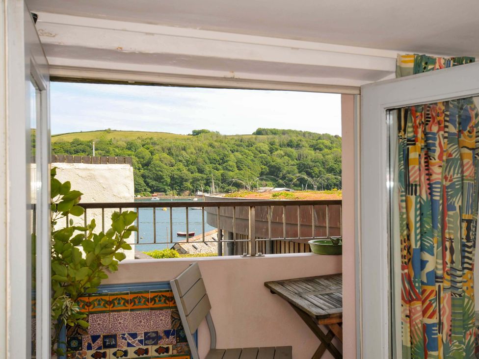 A balcony with a wooden table and chair overlooking a body of water and green hills at 5 Esplanade in Fowey