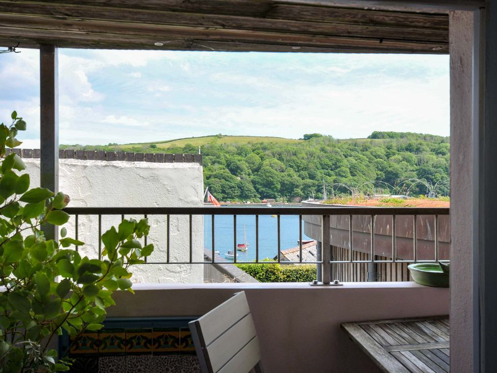 A balcony with a wooden table and greenery overlooking a river with boats and hills in the background at 5 Esplanade in Fowey