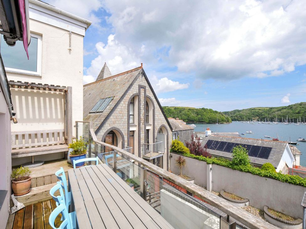 A balcony with wooden table and blue chairs overlooking a waterway with boats and green hills at 5 Esplanade in Fowey