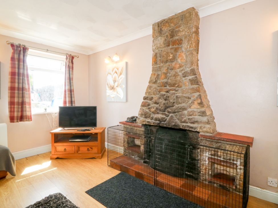 A living room with a stone fireplace and television at Llain Delyn near Capel Mawr near Malltraeth
