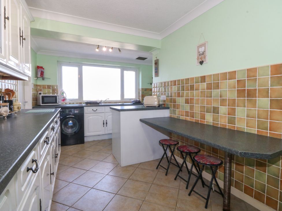 A kitchen with a washing machine and stools at Llain Delyn in Capel Mawr near Malltraeth
