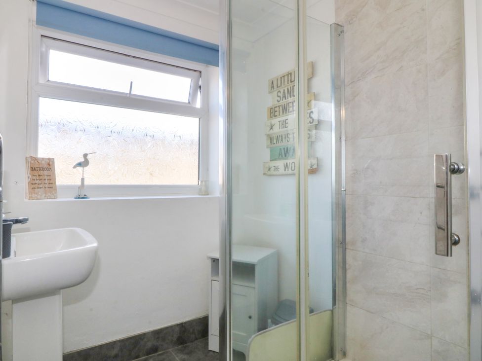 A bathroom with a sink, shower, and window at Llain Delyn, Capel Mawr near Malltraeth