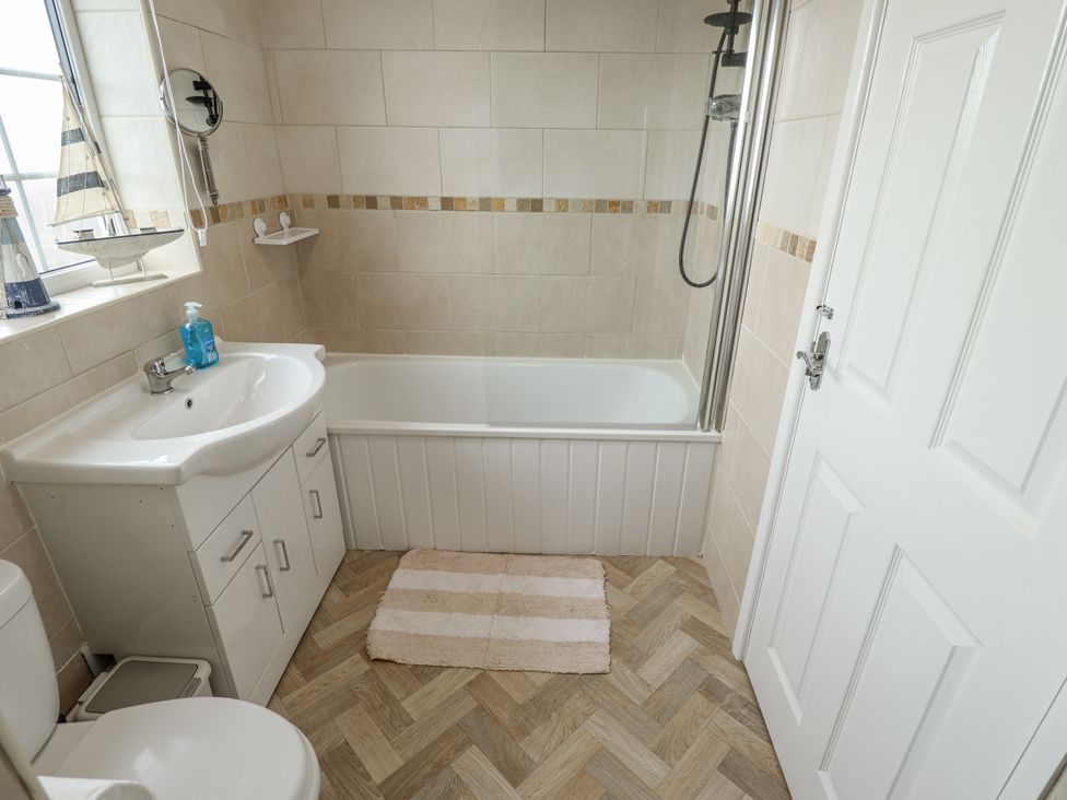 A bathroom with a bath tub, toilet, sink and mirror at 5 Links Court in Skegness