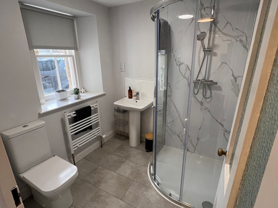 A bathroom with a toilet, shower, sink and radiator at 1 Links Place in Nairn