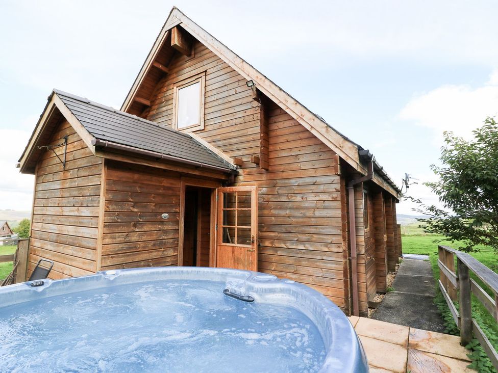 An outdoor view of a wooden cabin beside a hot tub at Pen Y Clawdd near Beggar's Bush